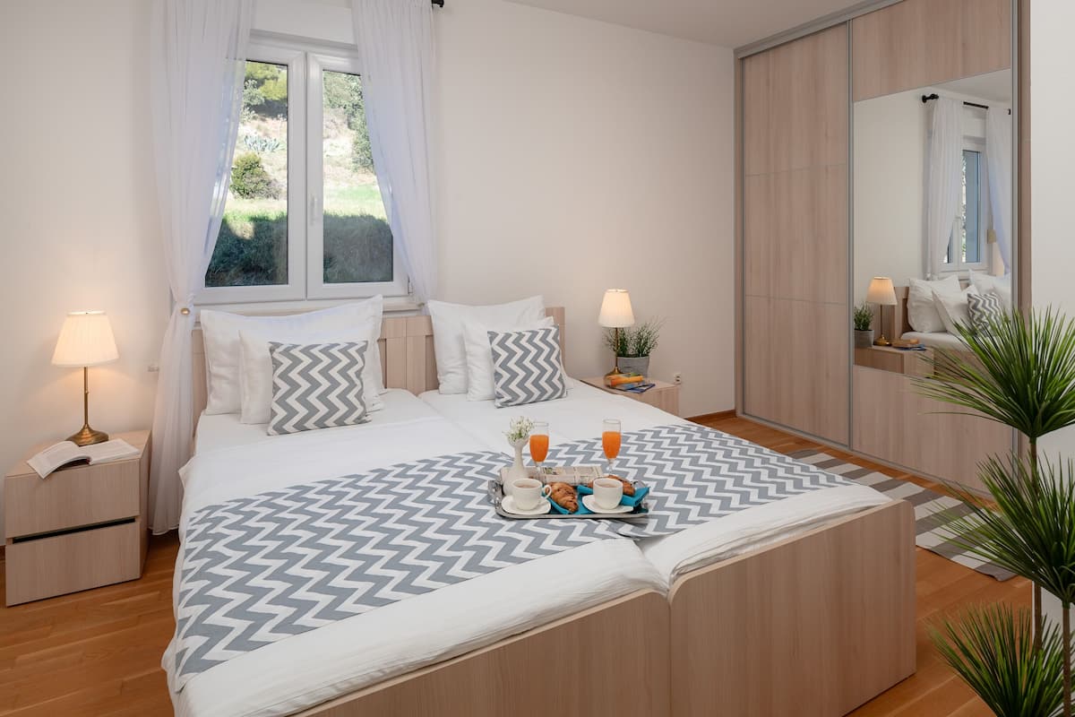 A neatly arranged bedroom with a bed, bedside tables, a bedside lamp, a tray with breakfast items, and a large mirror.