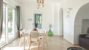 A dining area with a table and chairs, a vase with flowers, and a remote control on a side table. - Dimora il Mandorlo -The Plum tree private jacuzzi (Ostuni)