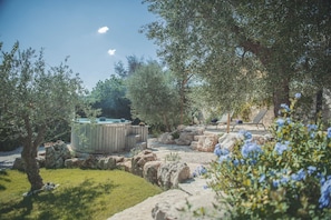 Un jacuzzi rodeado de rocas y follaje, con un banco de piedra y sillones de descanso al fondo.