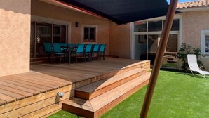 Eine überdachte Terrasse mit Holzboden, Sitzgelegenheiten im Freien und Blick auf das Haus.
