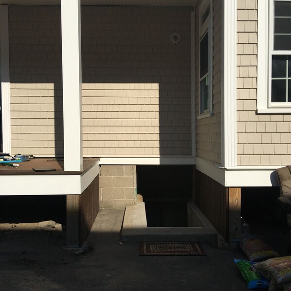 A corner of a house with a small enclosed porch area, a window, and a door leading to a basement.