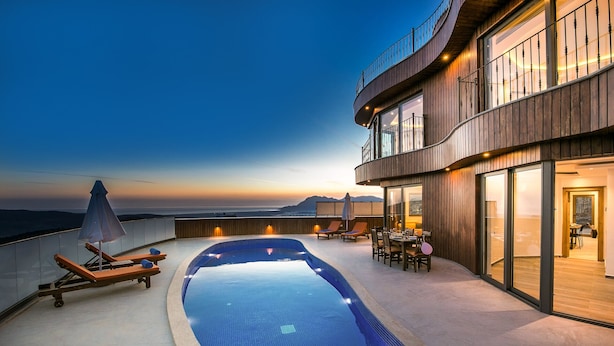 A rooftop infinity pool with lounge chairs and umbrellas, a dining area, and a view of the ocean at sunset. - Villas Bella (Kas)