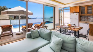 A modern living room with a sofa, dining table, and chairs, overlooking a pool and a scenic view. - Villas Bella (Kas)