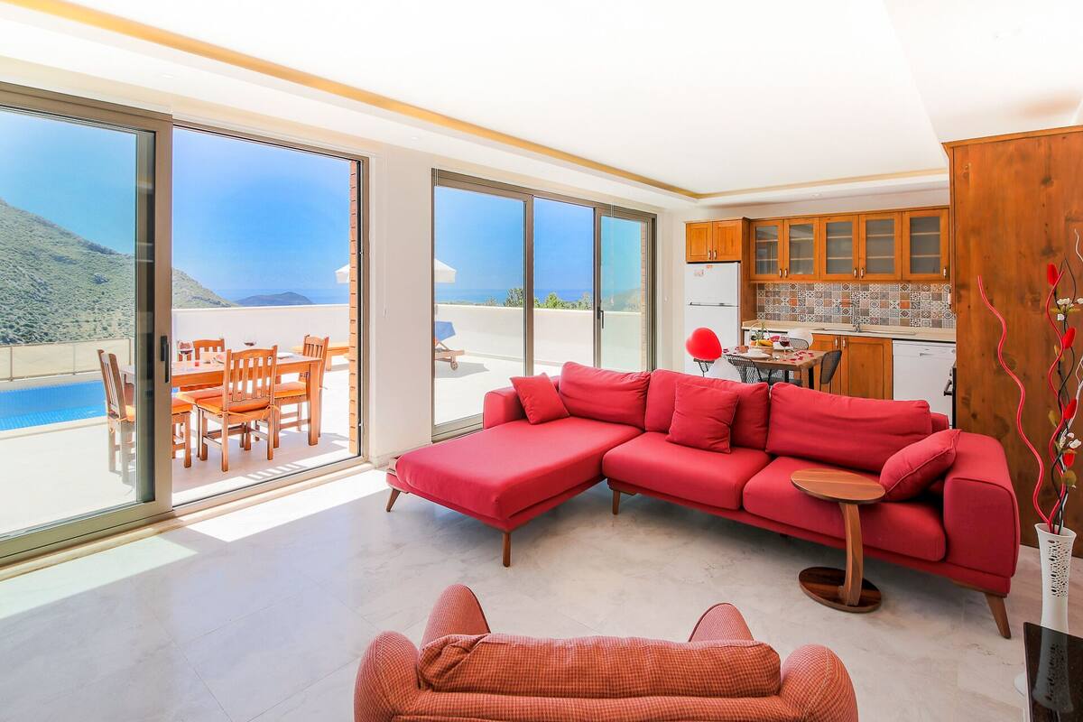 A modern living room with a red sectional sofa, a dining area with wooden chairs, and a kitchen with wooden cabinets.