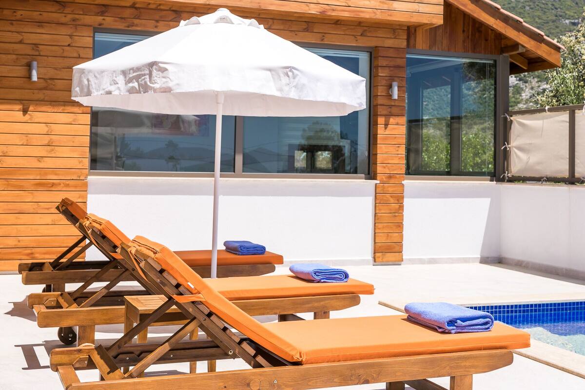 A poolside area with wooden lounge chairs and a white umbrella.
