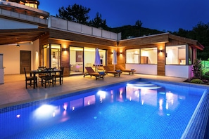 Une maison moderne dotée d’une piscine, d’un espace salon extérieur et d’un patio couvert.