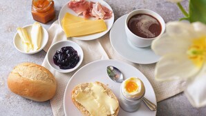 En frukostuppläggning med bröd, ost, skinka, sylt, kaffe och ett kokt ägg.