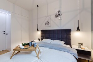 A modern bedroom with a bed, bedside tables, a wooden nightstand, a tray with snacks, and two wall-mounted lights.
