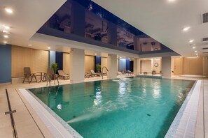 A large indoor swimming pool with multiple lounge areas and a high ceiling with skylights.