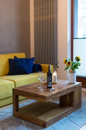 A wooden coffee table with a bottle and glasses, a candle, and a vase with sunflowers.