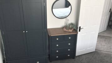 Een slaapkamer met een donkere houten garderobe, een kleinere dressoir, een spiegel en een witte deur.