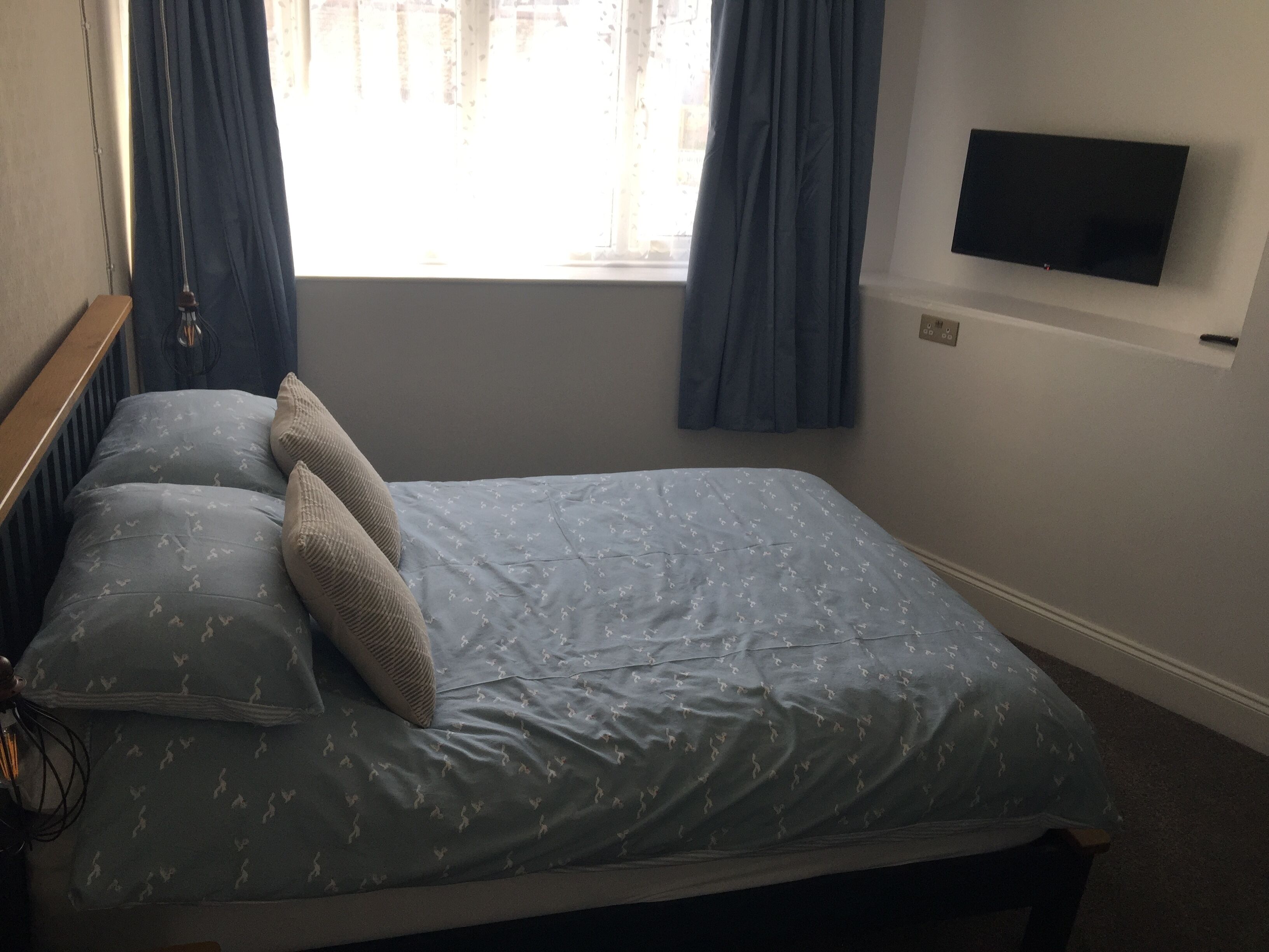 Une chambre à coucher avec un lit, un téléviseur fixé au mur et une fenêtre avec des rideaux.