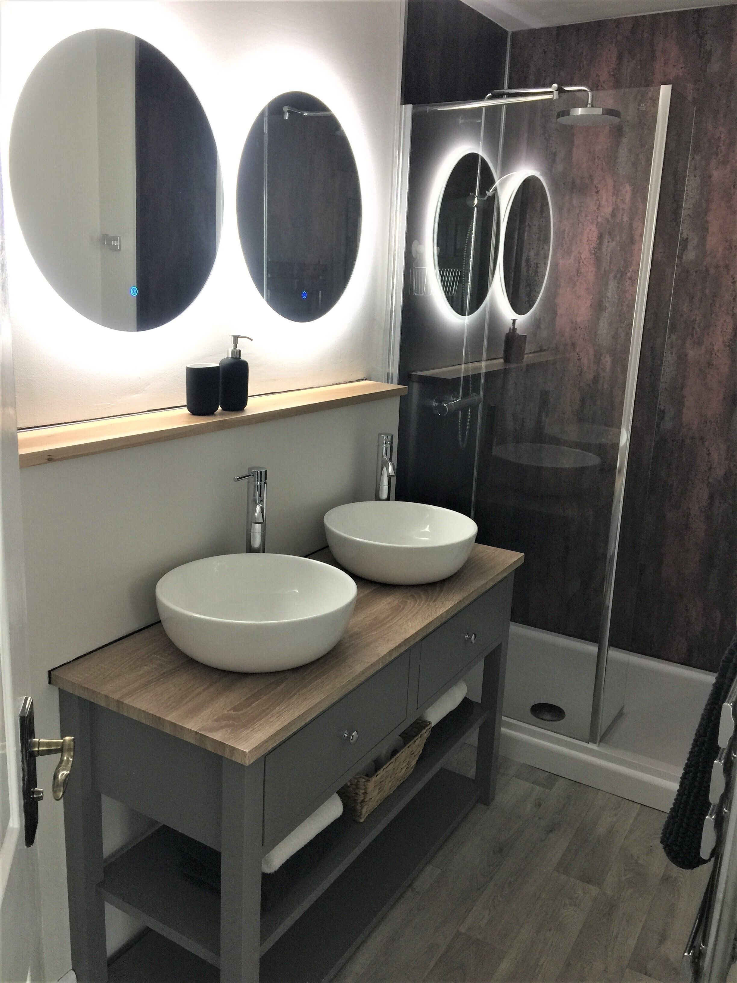 A modern bathroom with two round white sinks, a wooden vanity, and a glass-enclosed shower.