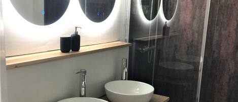 A modern bathroom with two round white sinks, a wooden vanity, and a glass-enclosed shower.