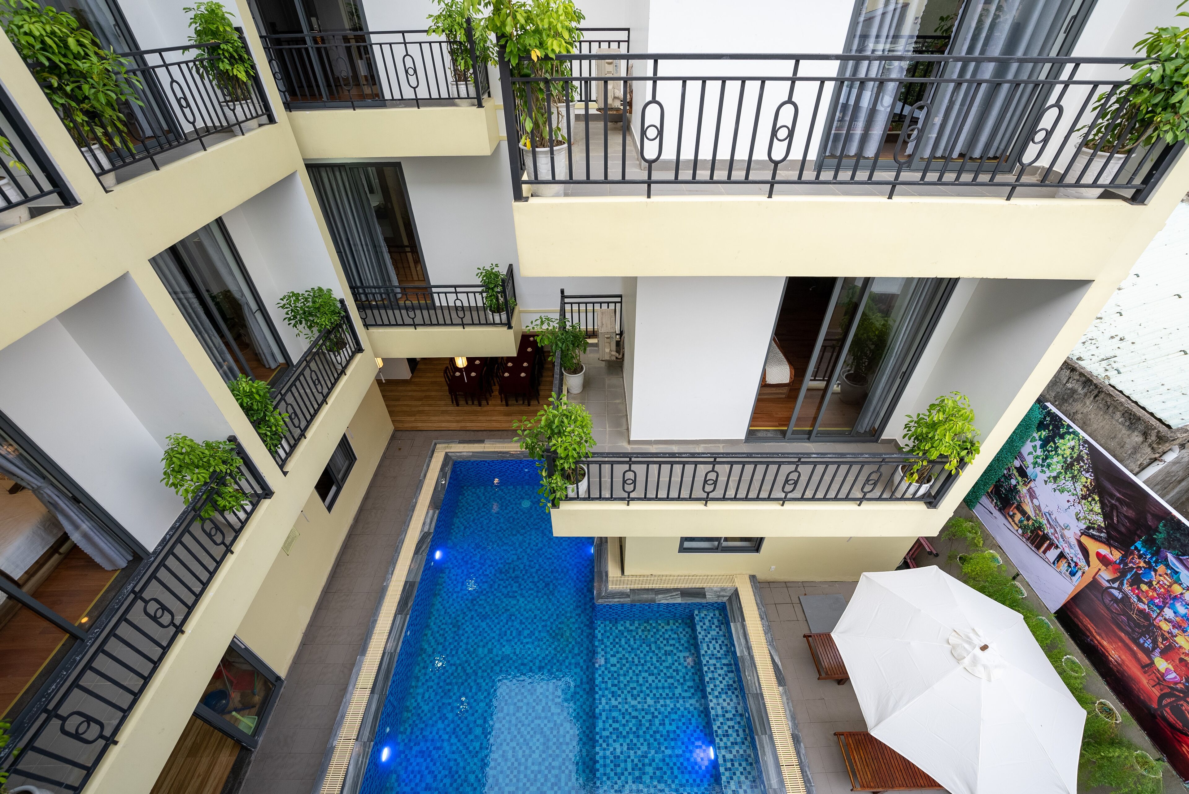 Edificio de varios niveles con piscina central, balcones con plantas y vistas a la piscina desde los pisos superiores.