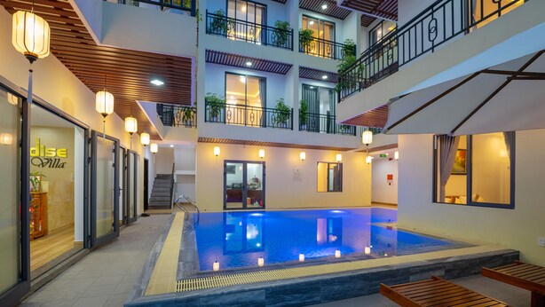A hotel atrium with a central pool, wooden benches, and a staircase leading to the upper floors. - Hoi An Paradise Villa (Da Nang)