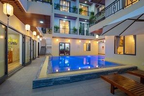 A hotel atrium with a central pool, wooden benches, and a staircase leading to the upper floors. - Hoi An Paradise Villa (Da Nang)
