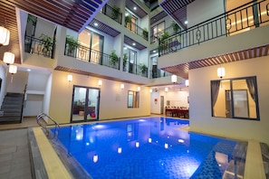 A multi-level indoor swimming pool with a tiled floor, railings, and potted plants on balconies. - Hoi An Paradise Villa (Da Nang)