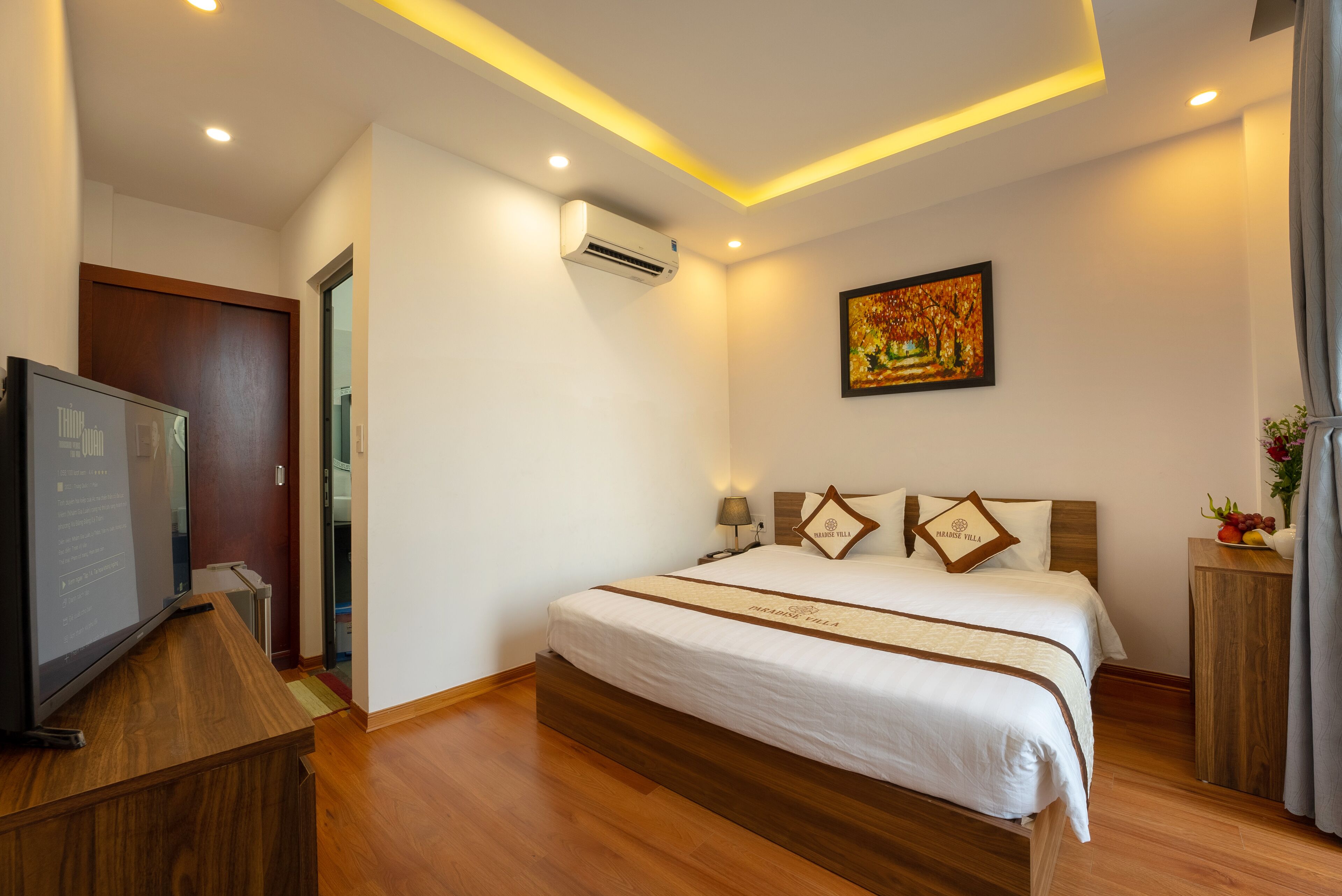 A hotel room with a large bed, a TV, an air conditioner, and a painting on the wall.
