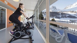 A person using an exercise bike in a room with large windows overlooking a snowy mountain landscape. - Belambra Clubs Gourette - Lou Sarri (Eaux-Bonnes)