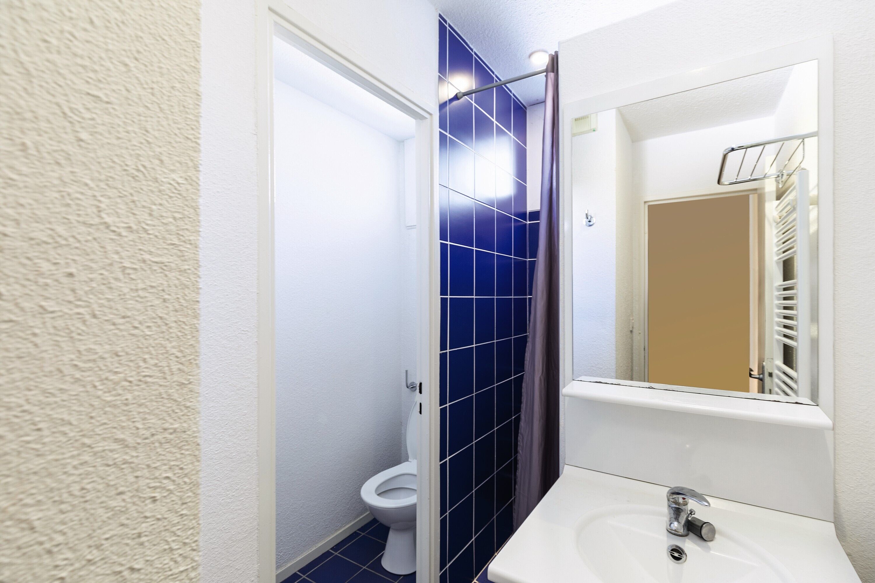Une salle de bain avec un lavabo blanc, un miroir et des murs recouverts de carreaux bleus.