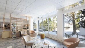 A modern interior with large windows, a wooden bookshelf, and several seating areas. - Belambra Clubs Gourette - Lou Sarri (Eaux-Bonnes)