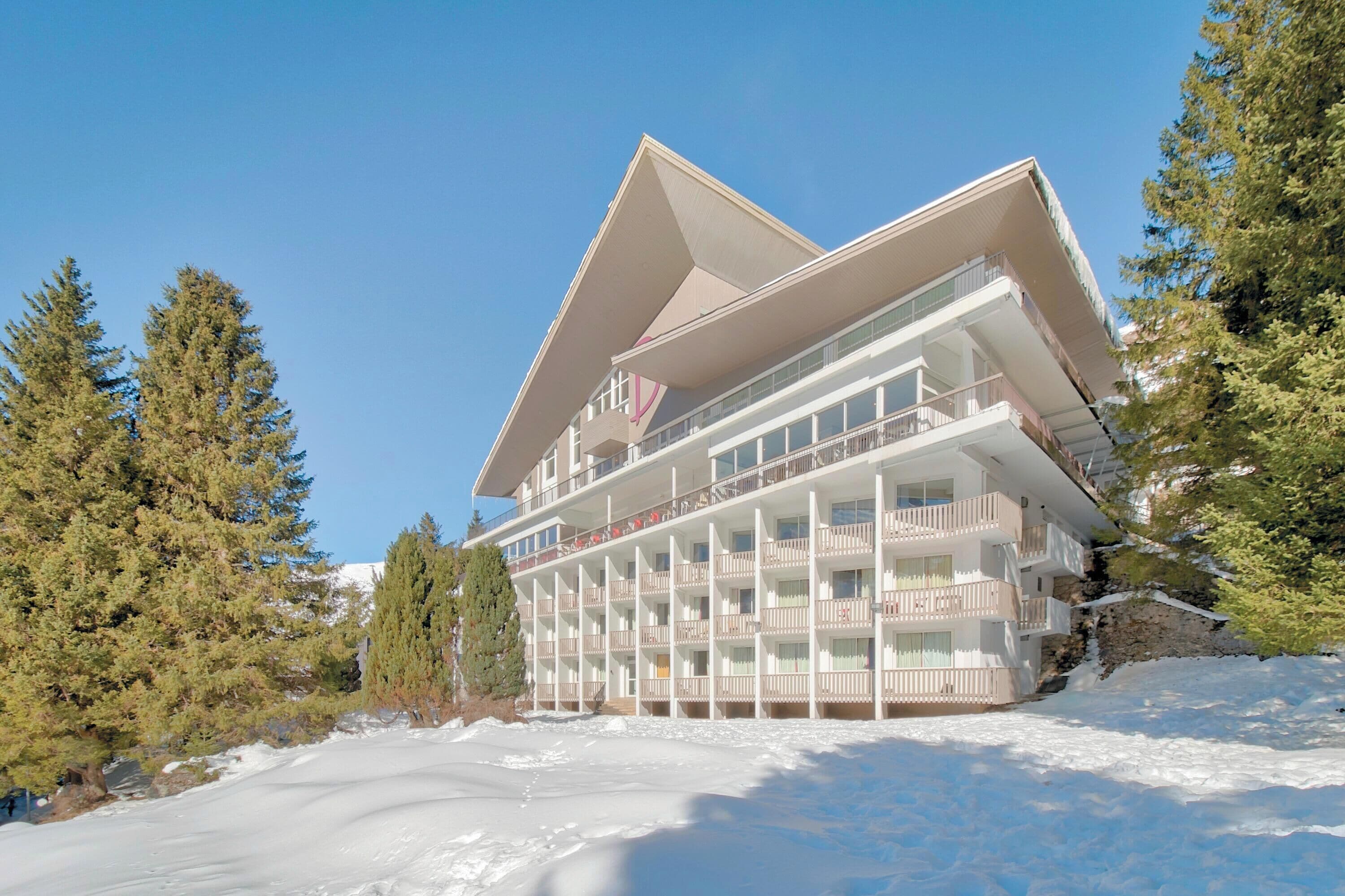 A multi-story hotel with balconies, surrounded by snow and trees.