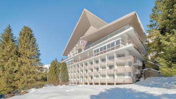 A multi-story hotel with balconies, surrounded by snow and trees.