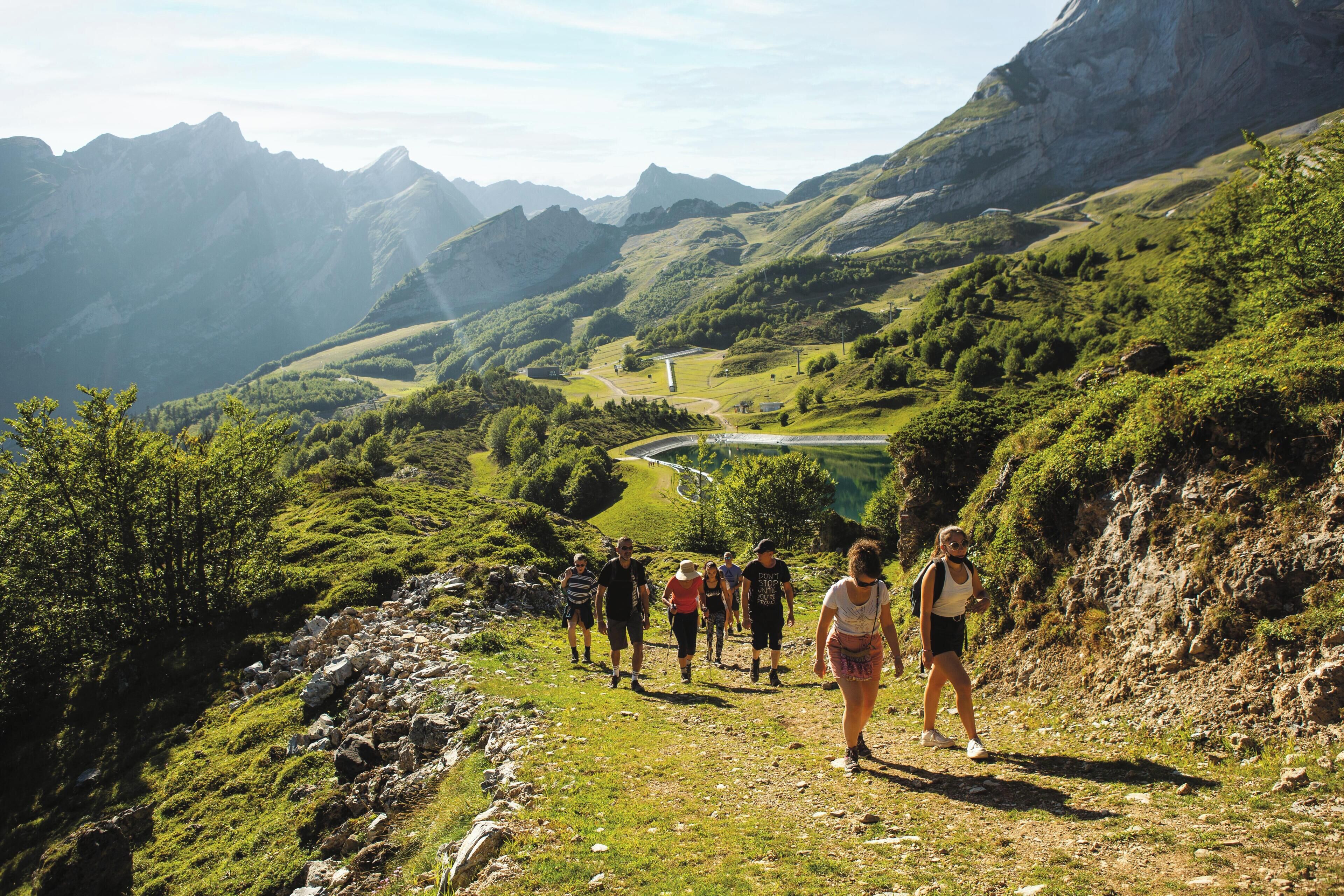A group of people hiking on a mountain trail with a valley and mountains in the background.