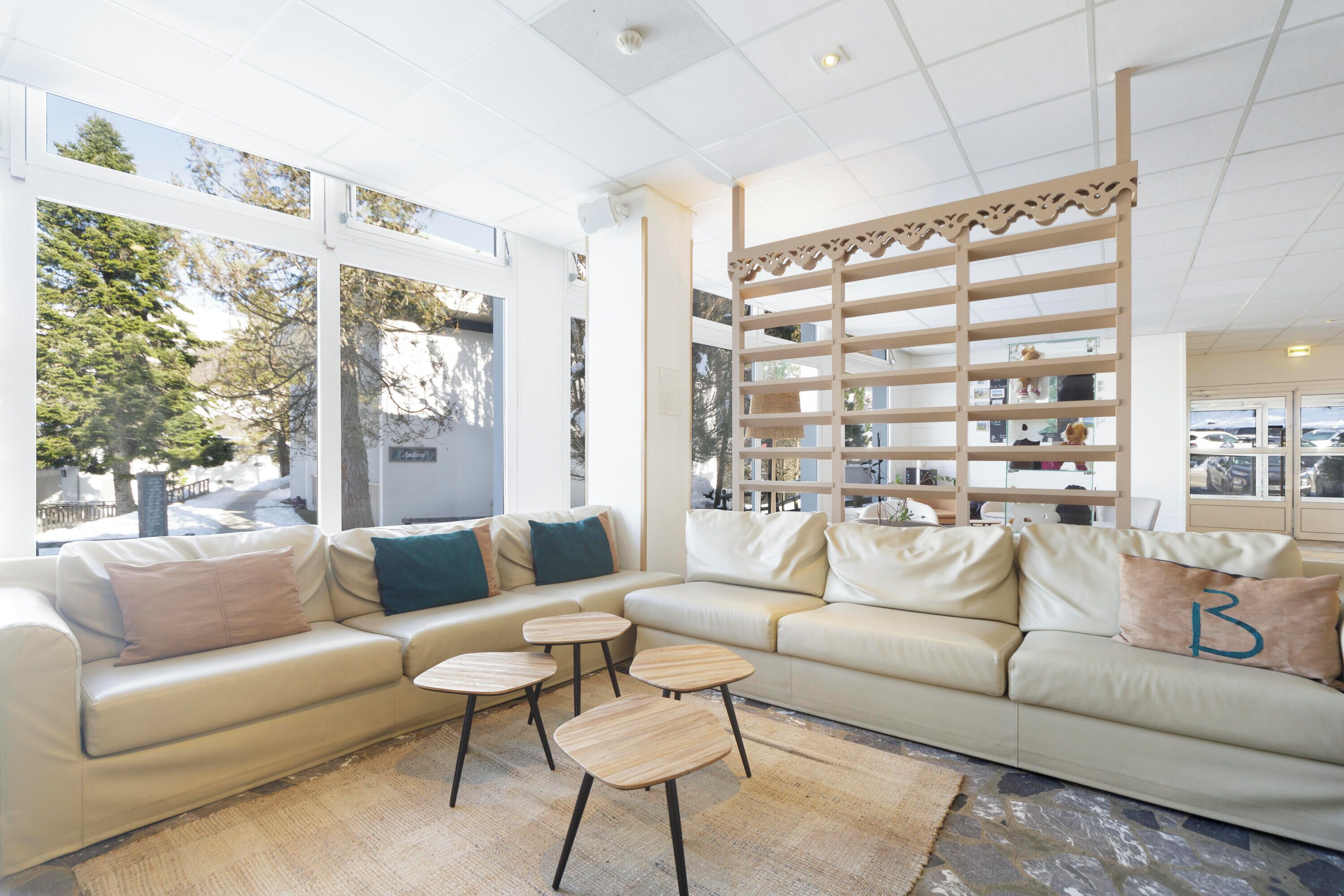 A modern living room with a beige sofa, two round wooden side tables, and a decorative wooden shelf unit.