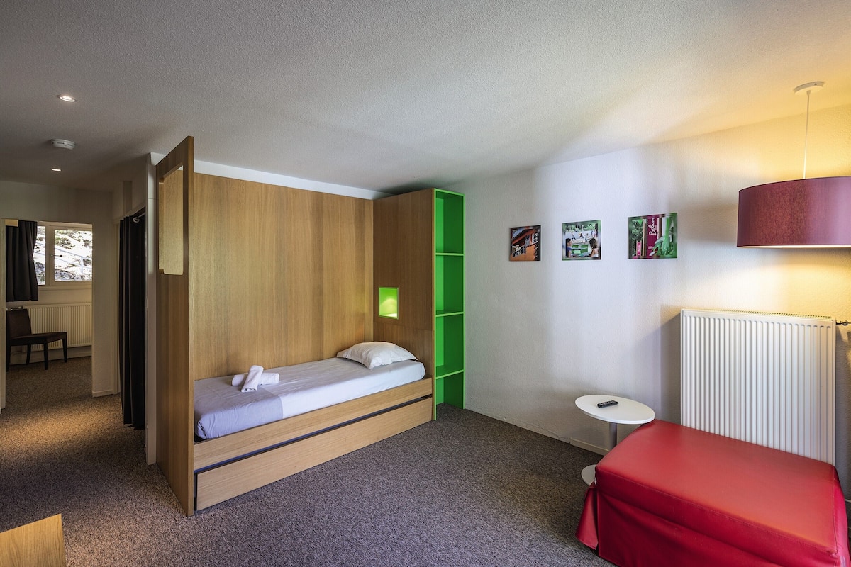 Een kleine kamer met een bed, een tafeltje, een radiator en een groen dressoir.