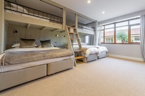 A bedroom with a bunk bed, a ladder, a desk, and a large window.