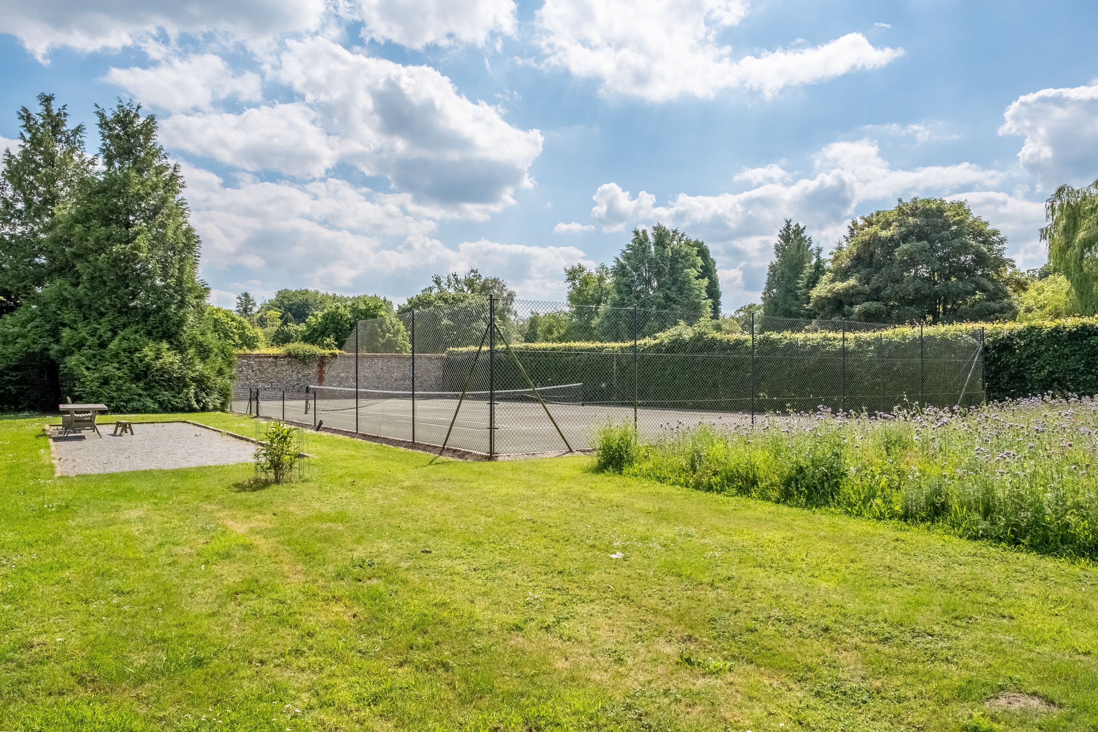 A fenced tennis court surrounded by lush greenery and trees.