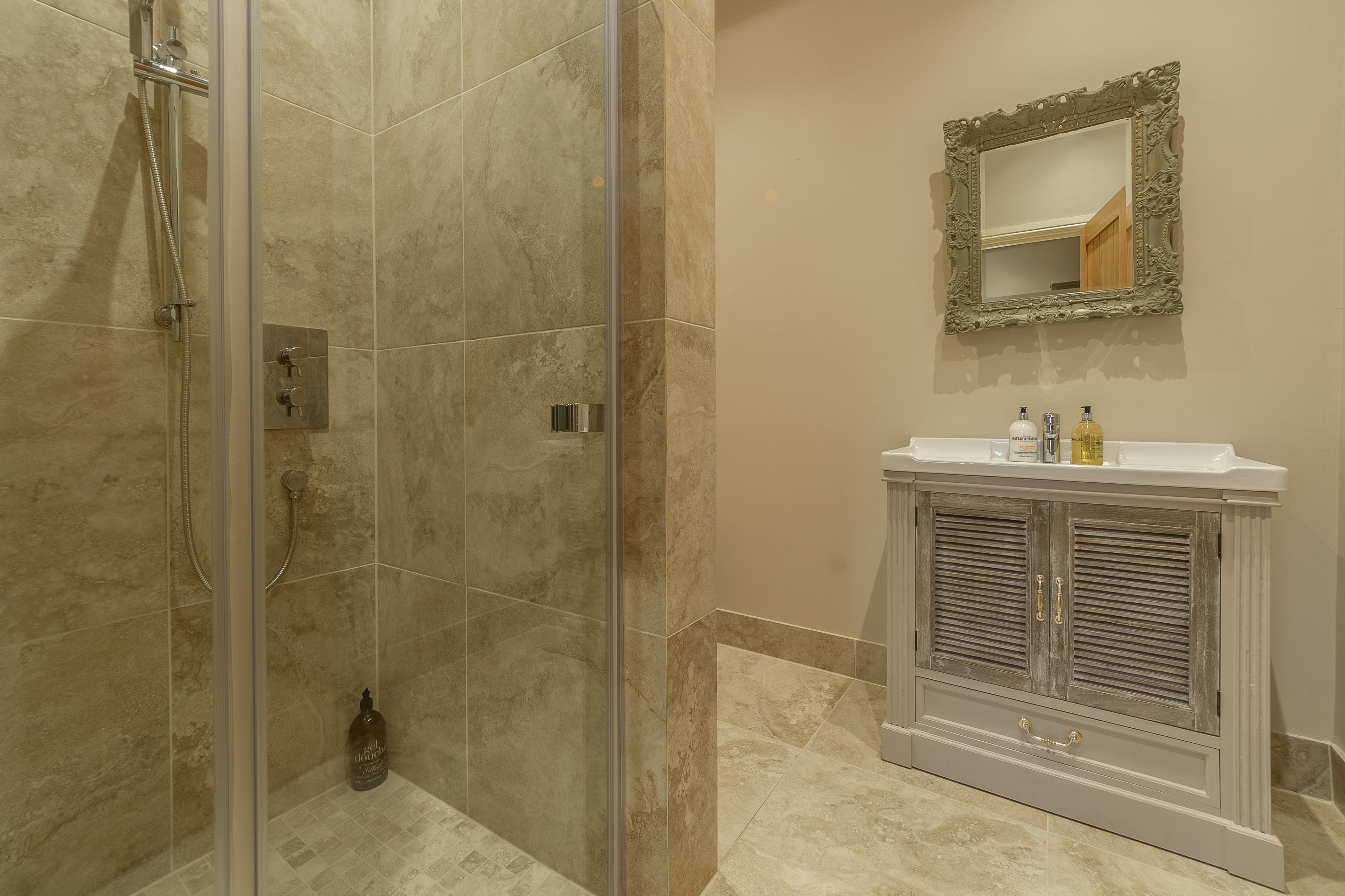 Une salle de bain avec une douche à parois de verre, un meuble-lavabo avec un miroir et un placard avec des tiroirs.