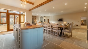 A spacious kitchen with a central island, a dining area with multiple chairs, and a stone-tiled floor. - Red Stag Lodge, Little Massingham, Norfolk (Little Massingham)