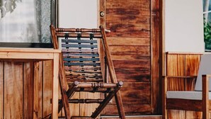 Une chaise en bois avec un dossier à lattes, placée sur une véranda.
