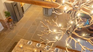 A dining area with a wooden table set for four, surrounded by a chandelier with antler-like branches and candles. - Hill Farm Massingham, Little Massingham, Norfolk (Little Massingham)