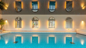 A large indoor swimming pool with clear blue water, surrounded by walls with arched windows and wall-mounted lights. - Hill Farm Massingham, Little Massingham, Norfolk (Little Massingham)