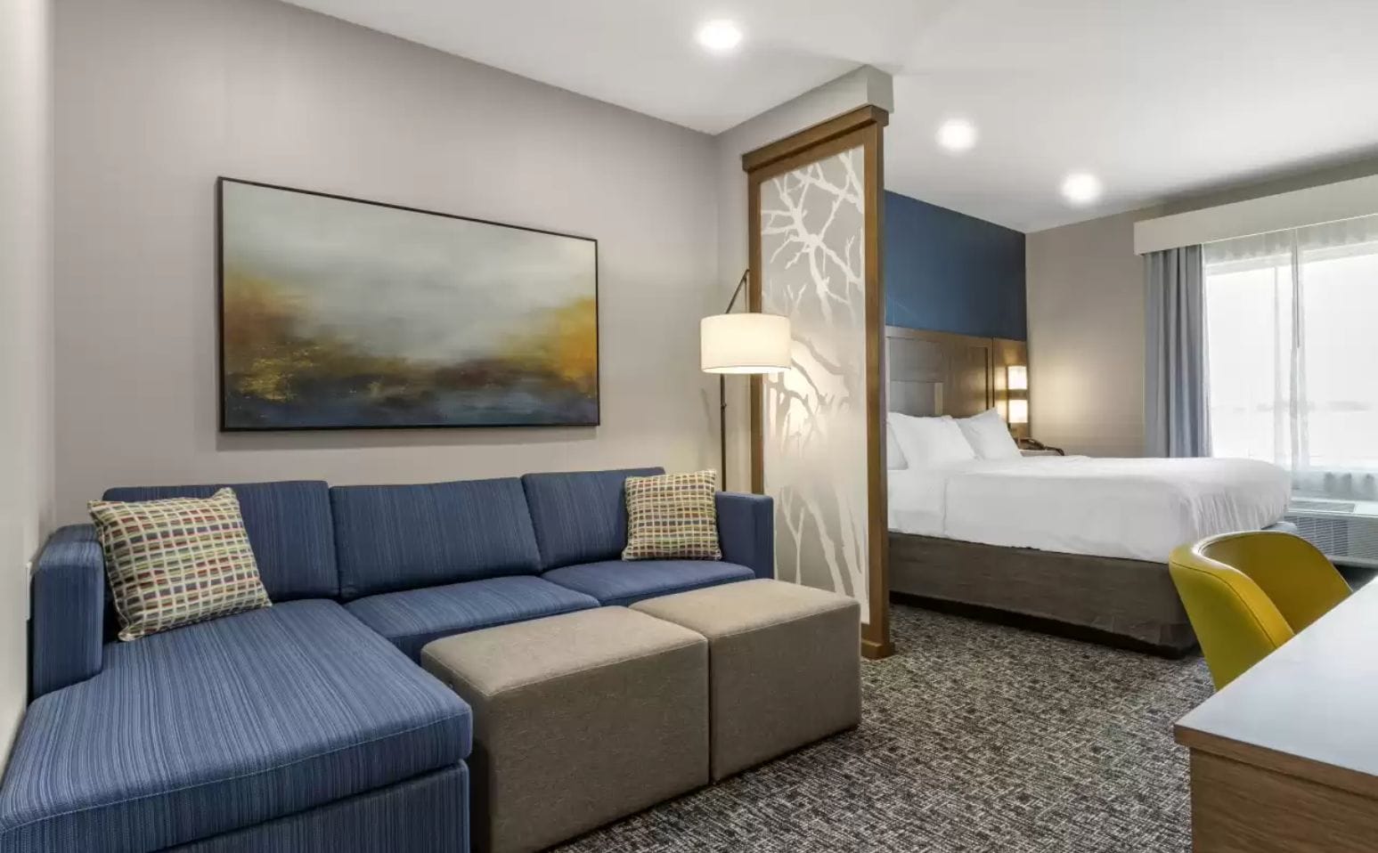 Quarto de hotel com sofá, cama, escrivaninha e uma grande janela.