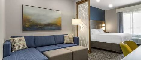 Quarto de hotel com sofá, cama, escrivaninha e uma grande janela.