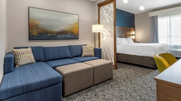 Una habitación de hotel con sofá modular, cama, escritorio y una ventana grande.