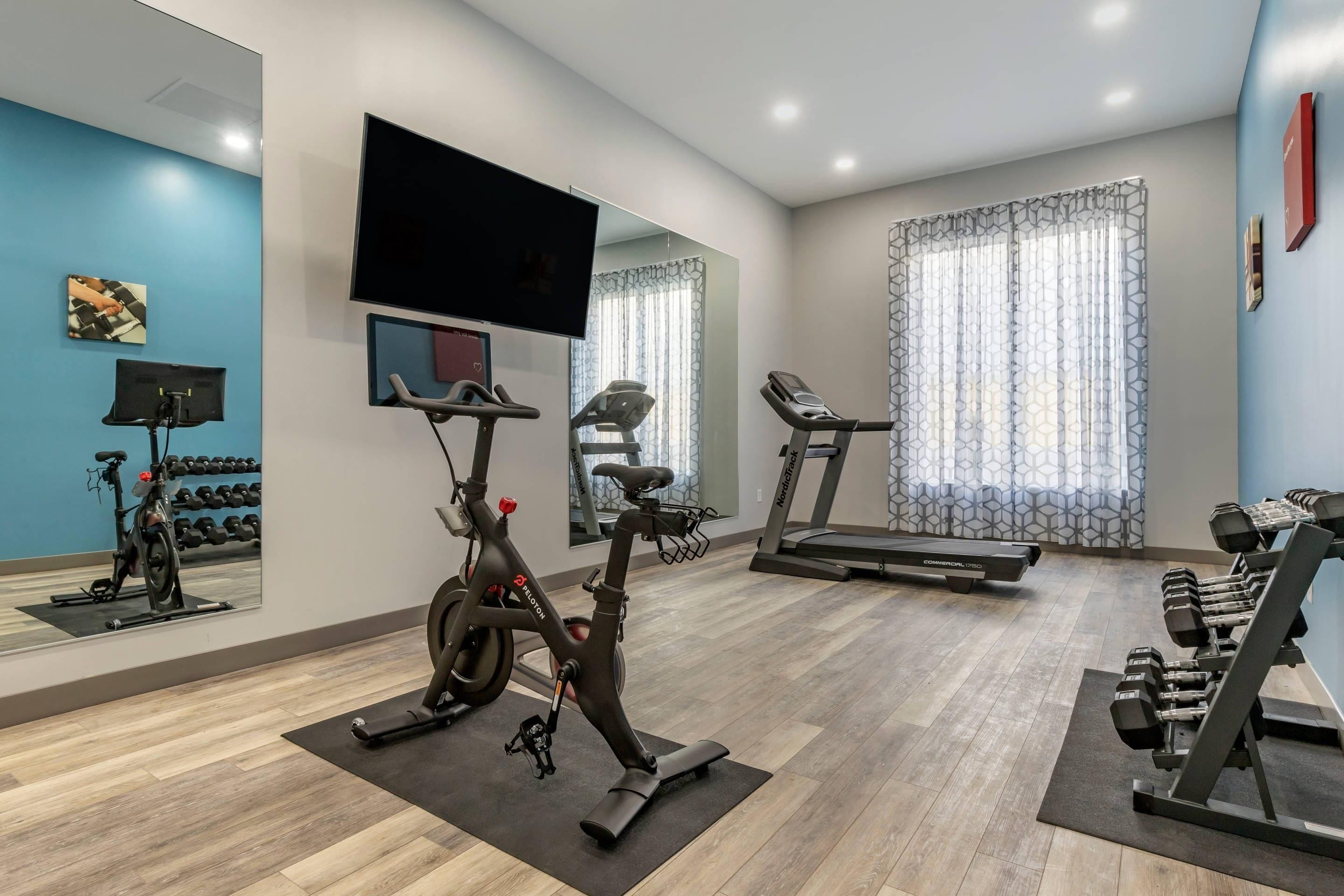 Un gimnasio en casa con equipo de ejercicio, un televisor y un espejo.
