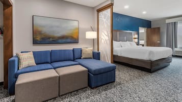 A hotel room with a blue sofa, a bed, a large abstract painting, and a patterned carpet.