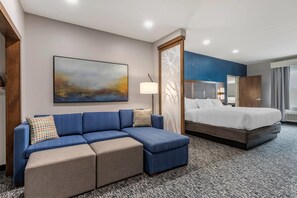Une chambre d’h ôtel avec un canapé bleu, un lit, un grand tableau abstrait et une moquette à motifs.