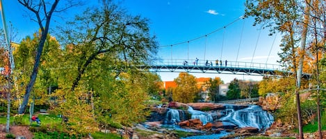 Eine Hängebrücke über einem Wasserfall, mit Bäumen und blauem Himmel.