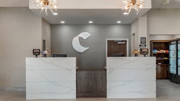 Un hall d’accueil d’hôtel avec un comptoir de réception en marbre, une grande décoration murale en forme de croissant de lune et un mini-bar.