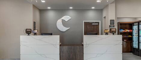 Zona de recepción de un hotel con mostradores de mármol, una decoración de gran luna colgante y un minibar.