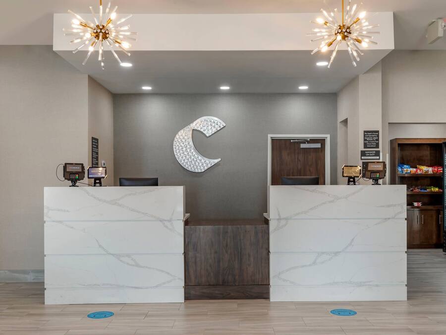 Un hall d’accueil d’hôtel avec un comptoir de réception en marbre, une grande décoration murale en forme de croissant de lune et un mini-bar.