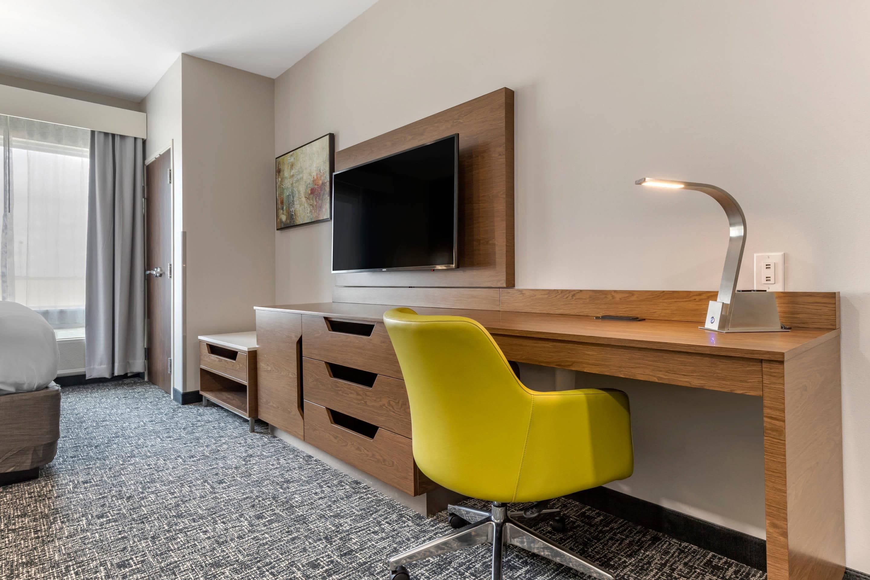 A hotel room with a desk, a television, a chair, and a lamp.