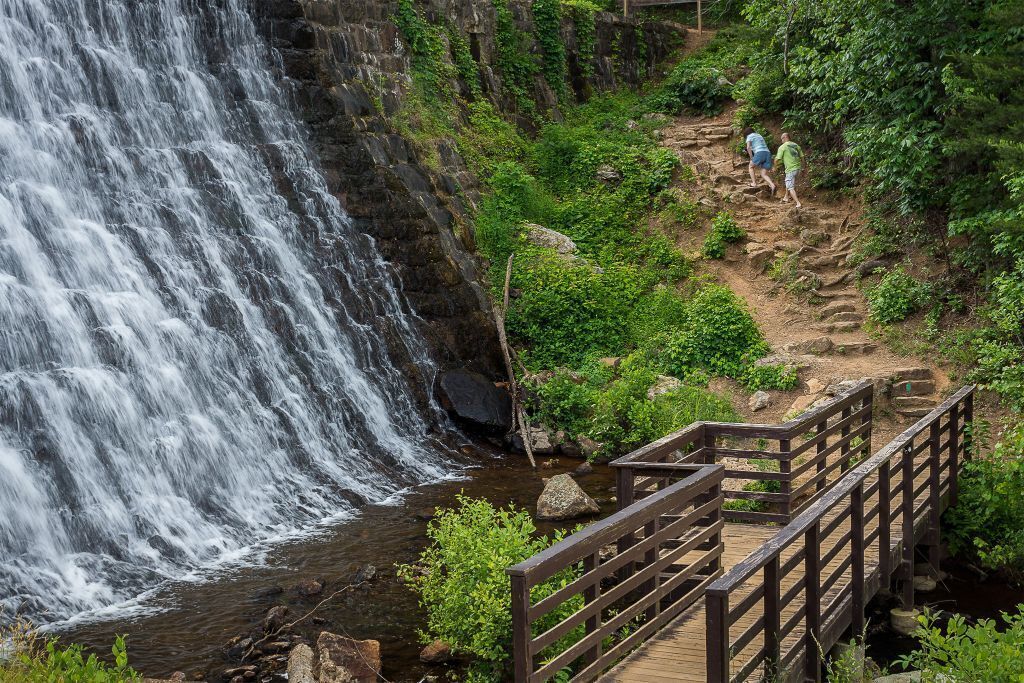 A wooden bridge over a waterfall with lush greenery around.